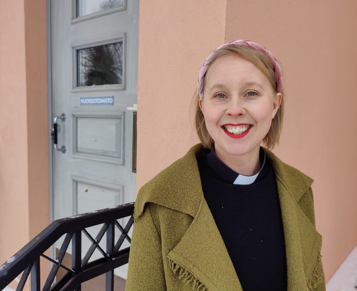 Prästen Anna Kinnunen framför en dörr.