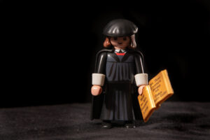 Playmobile man med svarta kläder, bland annat en svart kåpa. I handen har han nya testamentet på tyska.