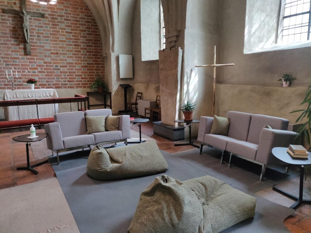Ett kyrkorum med ett altare, ett krucifix, två soffor och kuddar på golvet.